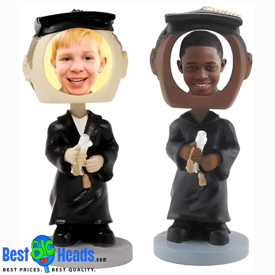 Two custom bobbleheads of young graduates dressed in black graduation gowns and caps, holding diplomas. The bobbleheads feature oversized heads with cutouts for personalized photos.